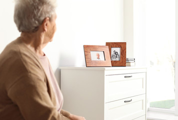 Elderly woman looking at framed family portraits indoors