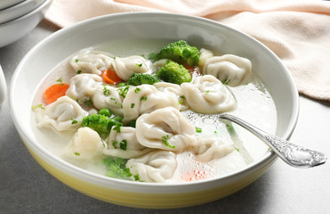 Bowl of tasty dumplings in broth with spoon on table, closeup