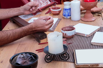 foreground of the hands of a craftsman using paintbrushes and tint to decorate tiles using traditional and craft techniques
