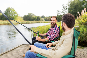 leisure and people concept - male friends fishing and drinking beer on lake