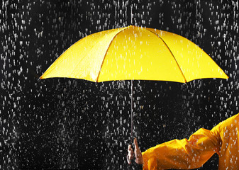 Woman holding bright umbrella under rain on dark background, closeup