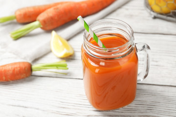 Mason jar with fresh carrot juice on white wooden table, space for text