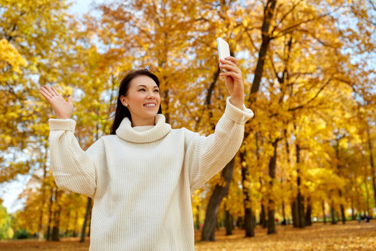 season, technology and people concept - beautiful happy woman taking selfie or making video call on smartphone at autumn park
