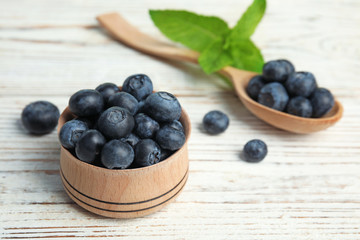 Wooden bowl and spoon of tasty blueberries on white table