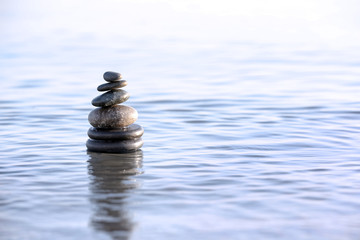 Stack of dark stones in sea water, space for text. Zen concept