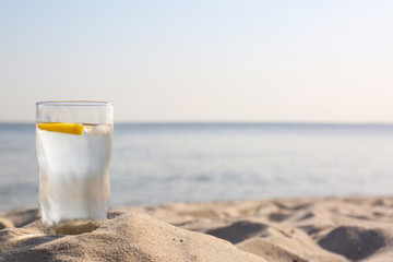Sandy beach with glass of refreshing lemon drink on hot summer day, space for text