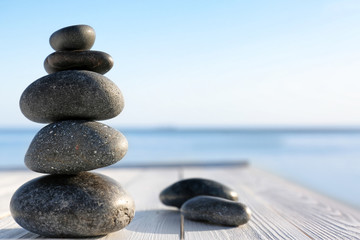 Stack of dark stones on wooden deck near sea, space for text. Zen concept
