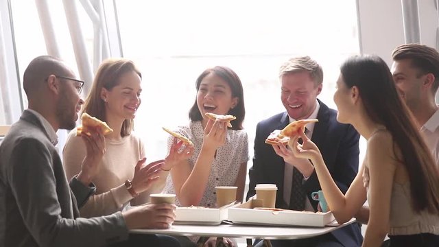 Happy multicultural business team talking laughing eating pizza in office