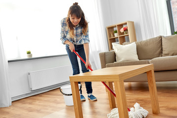 people, housework and housekeeping concept - happy asian woman or housewife with mop cleaning floor under table at home
