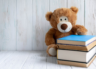 Photo of a stack of books with a bear and a place for an inscription on a wooden background. Back to school concept. Kids banner for text with books and bear. Concept on the topic of study