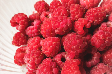 Close-up ripe juicy and delicious raspberry in a plastic transparent dish on a light background. Saturated healthy food