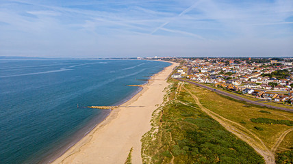 A beautiful aerial  seaside view with sandy beach, crystal blue water, groynes (breakwaters) and green vegetation dunes along a town under a majestic blue sky and white clouds