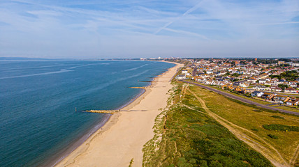 A beautiful aerial  seaside view with sandy beach, crystal blue water, groynes (breakwaters) and green vegetation dunes along a town under a majestic blue sky and white clouds