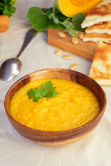 Roasted pumpkin and carrot soup with cream and pumpkin seeds on white wooden background. Copy space