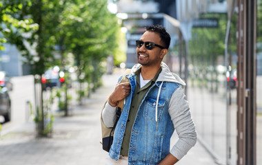 travel, tourism and lifestyle concept - smiling indian man in sunglasses with backpack on city street