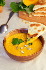 Roasted pumpkin and carrot soup with cream and pumpkin seeds on white wooden background. Copy space