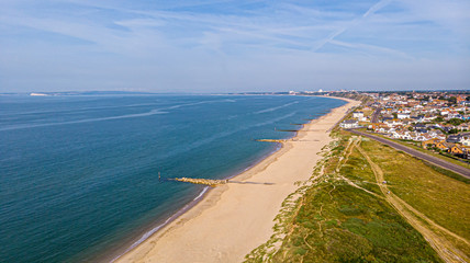 A beautiful aerial  seaside view with sandy beach, crystal blue water, groynes (breakwaters) and green vegetation dunes along a town under a majestic blue sky and white clouds
