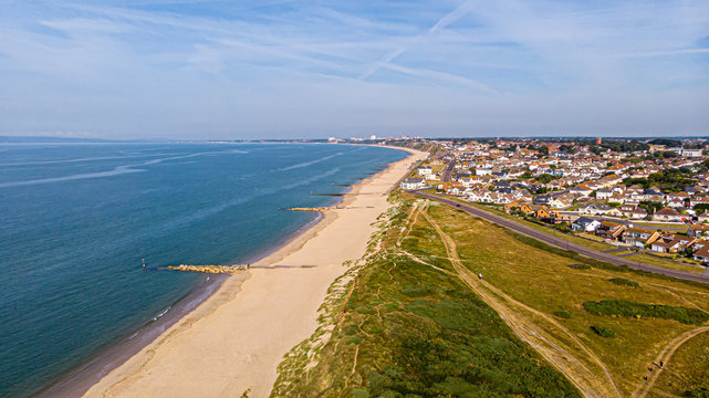 A beautiful aerial  seaside view with sandy beach, crystal blue water, groynes (breakwaters) and green vegetation dunes along a town under a majestic blue sky and white clouds