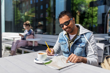 travel, tourism and people concept - indian man with map, notebook and coffee at street cafe in city