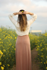 Beautiful woman on yellow flowers field with dark cloudy sky