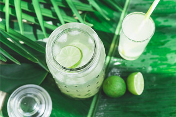Cold fresh lemonade drink with lime slice and ice cubes in a jar on a tropical background