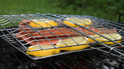 Grilling salmon with lemon slices on charcoal grill with gridiron.
