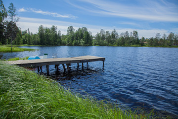 Fototapeta na wymiar Simple wooden jetty by the lake with high green grass in the foreground