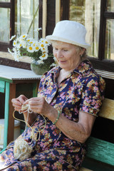 Portrait of an elderly woman with knitting needles. Summer sunny evening.