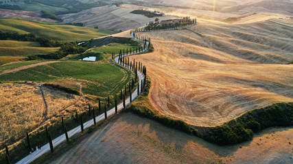Aerial view of Tuscany landscape, Asciano villa, curved road with cypress trees, field at summer sunset. Siena, Italy.
