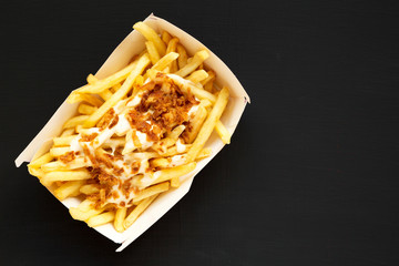 French fries with cheese sauce and onion in a paper box on a black background, top view. Flat lay, overhead, top view. Copy space.