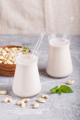 Organic non dairy cashew milk in glass and wooden plate with cashew nuts on a gray concrete background.