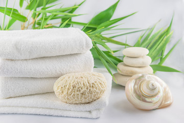 Obraz na płótnie Canvas Spa concept. White towels, seashell, massage stones and bamboo stems on the white background close up