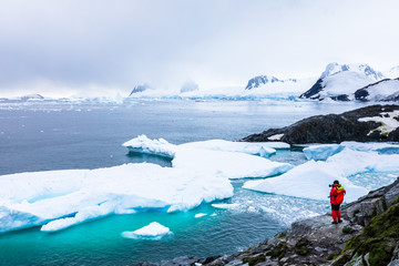 Tourist taking photos of amazing frozen landscape in Antarctica with icebergs, snow, mountains and glaciers, beautiful nature in Antarctic Peninsula with ice