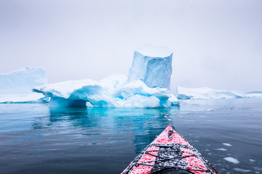 Kayaking between icebergs on a red kayak in Antarctica, POV (point of view) photo with frozen white landscape and blue ice, amazing scene in Antarctic Peninsula, extreme activity