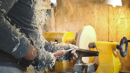 Carpenter cuts wood by graver. Woodworker handles wood by bench. Making beautiful wooden handmade dish. Craftsman works with workpiece in workshop. Creation of unusual platter.