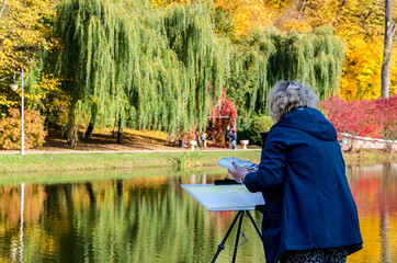 an elderly woman paints a picture looking at the bright autumn landscape