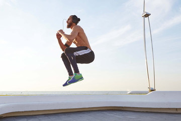 Obraz na płótnie Canvas Photo of young bearded jumping guy with fit athletic body,doing morning exercises, has muscular body shape, listening music on headphones.