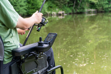 closeup of a man in a electric wheelchair fishing at the beautiful pond in natue on a sunny day