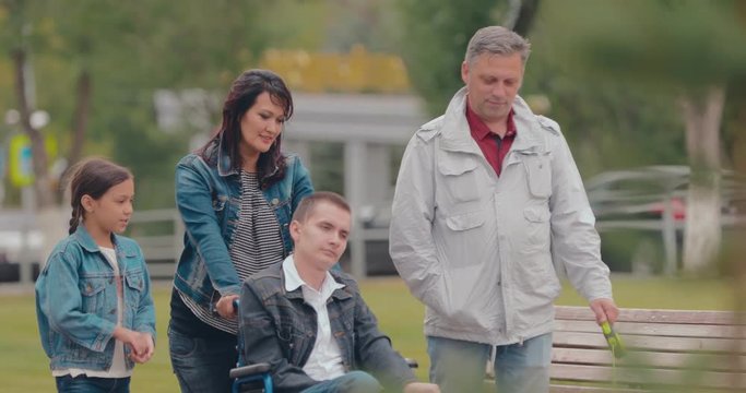 Parents go with children in the city. Guy in a wheelchair goes with his parents and sister along the avenue, a dog runs alongside.