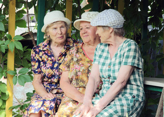 Three elderly women, close friends, sit on the summer terrace of their village house and talk to each other.