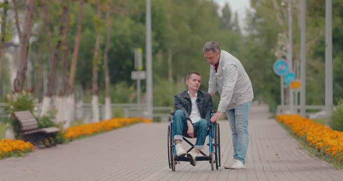 Young man gets up from the wheelchair and walks over. Father helps his son get up from the wheelchair and walk.
