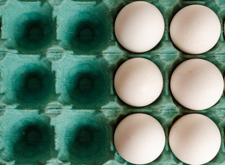 white eggs arranged together to the right side of a green egg carton with empty spaces on the left side.