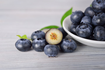 whole and half cut fresh blueberries in white plate and on wooden gray background