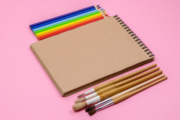 Watercolour brushes, Coloured pencils, notebook isolated on pink background for mockup. Flat lay, top view. Concept: back to school.