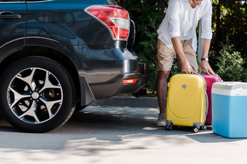 cropped view of bearded man standing near yellow luggage near car