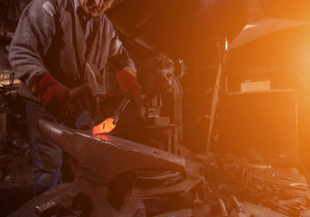 blacksmith manually forging the molten metal with sunlight through the windows