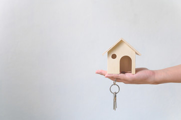 Hand holding wooden house and home keychain. Property investment and house mortgage financial real...