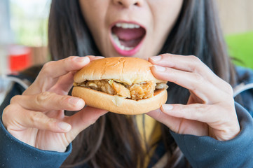 Young Asian woman holding a piece of small cheese burger in her hand. Hamburgers are sold at fast-food restaurants.