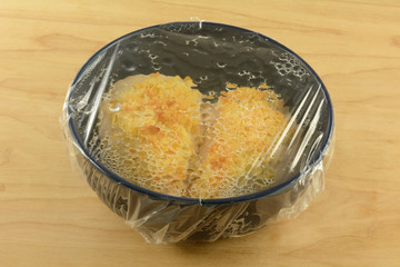 Refrigerated chicken breast cheese and bread crumbs crust left overs with plastic wrap over blue...