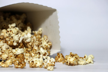 Heap of chocolate and caramel popcorn from paper box on the white floor.